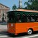Trolley filled with passengers in front of a brick building with a statue